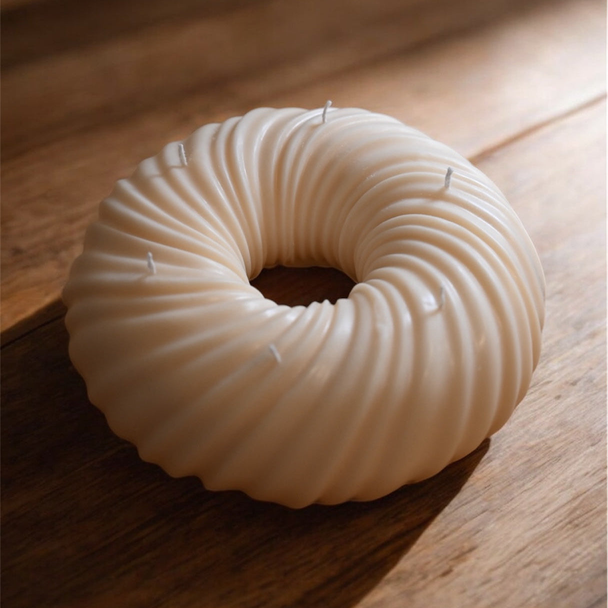 Decorative bundt cake candle on a wooden table highlighting sculptural ridges and handmade soy wax texture.
