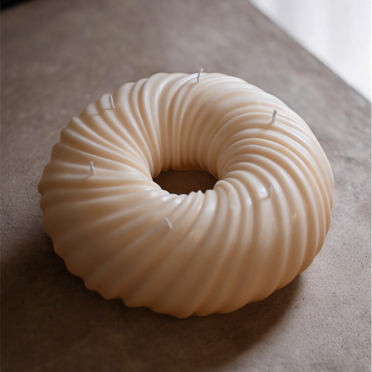 Neutral toned bundt cake sculptural candle made from soy wax displayed on a minimal surface as modern home decor.
