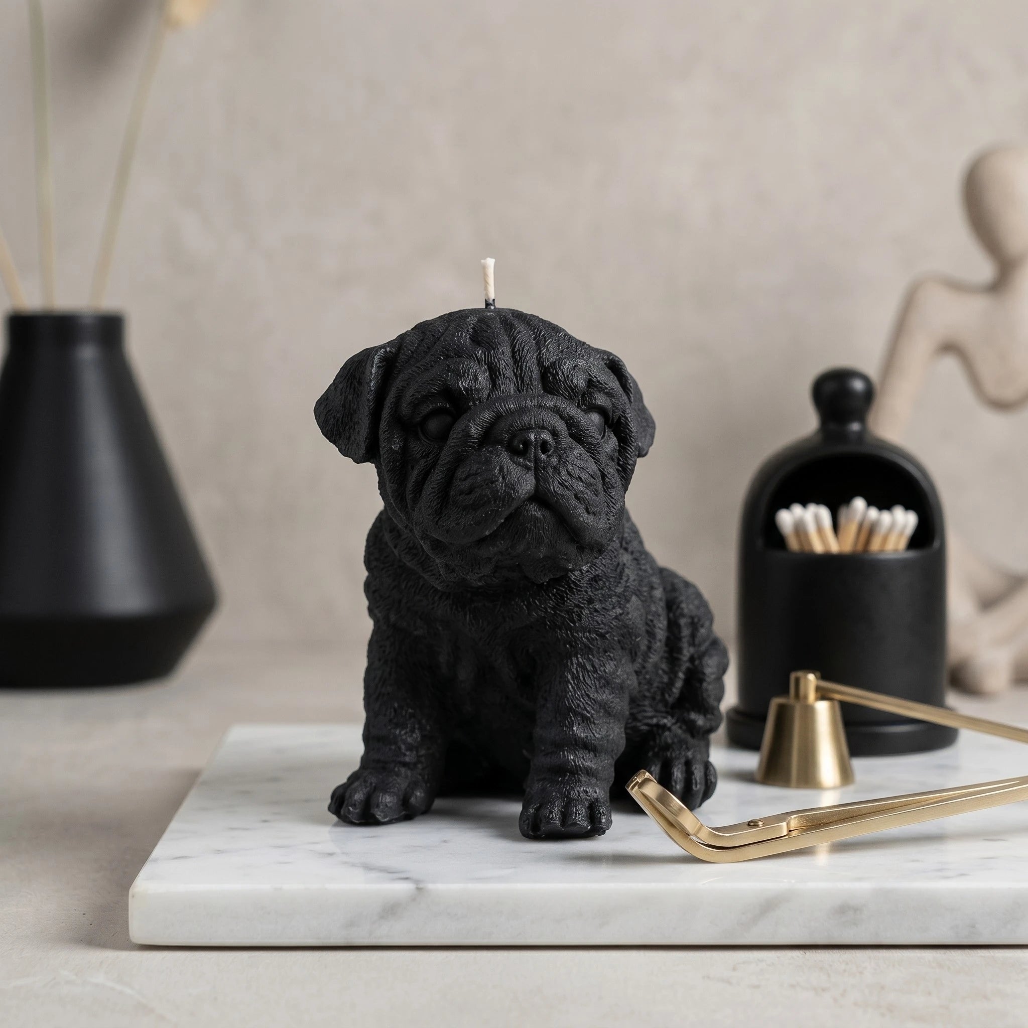 Black English Bulldog puppy candle by House of Wick on a marble surface with a gold snuffer.