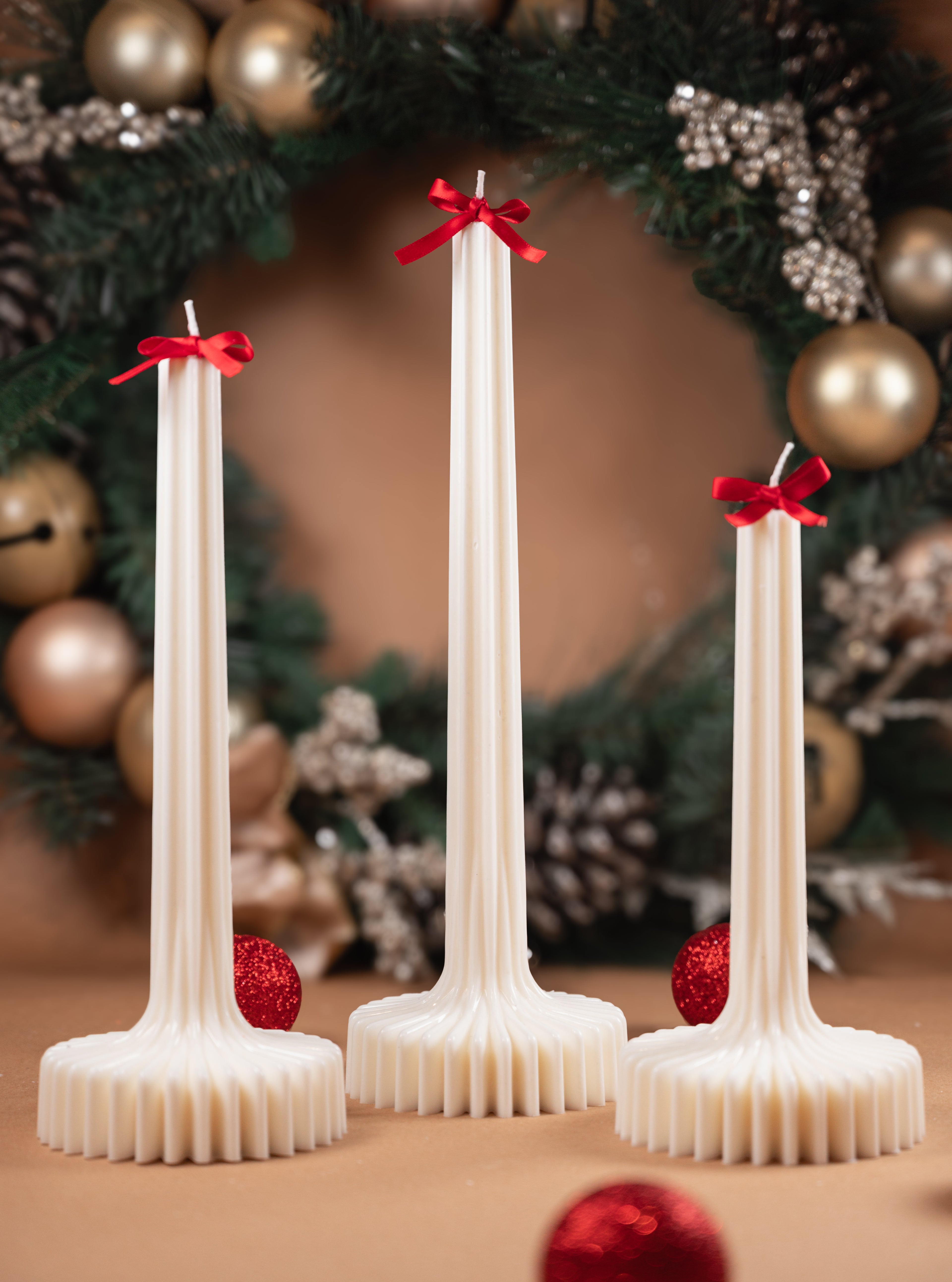 Fluted vase sculptural candles styled with red bows and holiday wreath creating elegant festive home decor centerpiece.