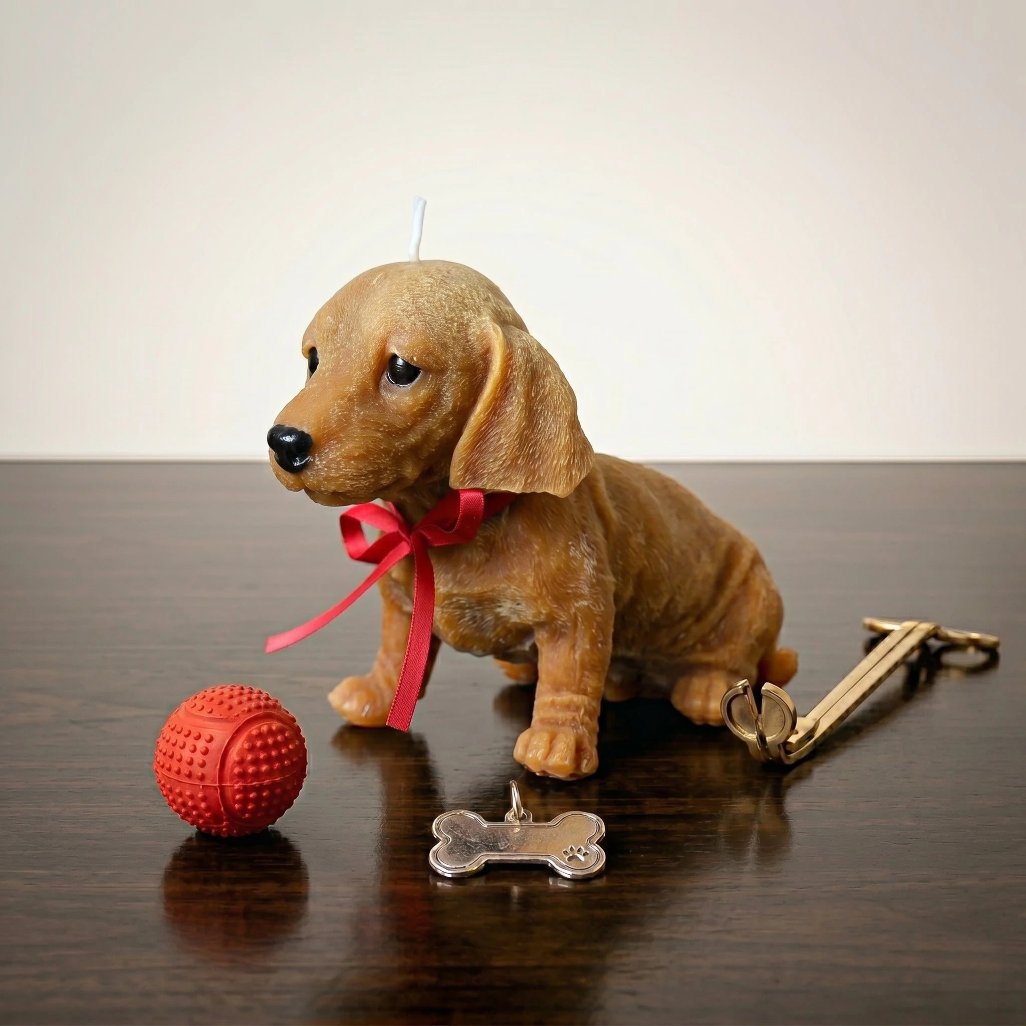 Golden dachshund puppy candle with red ribbon on dark table product shot