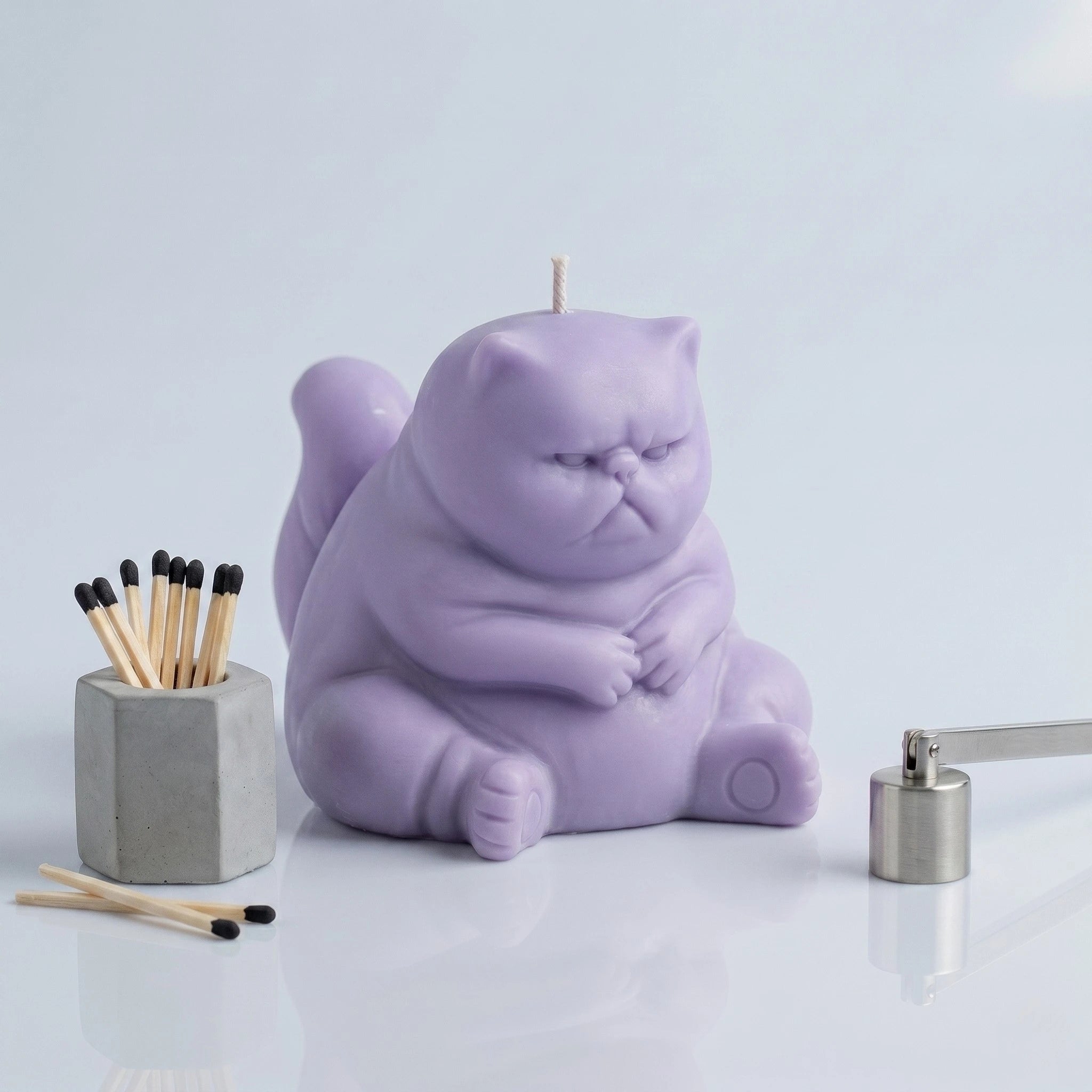 Pastel lavender chubby cat candle with folded paws on clean background with match holder and wick trimmer