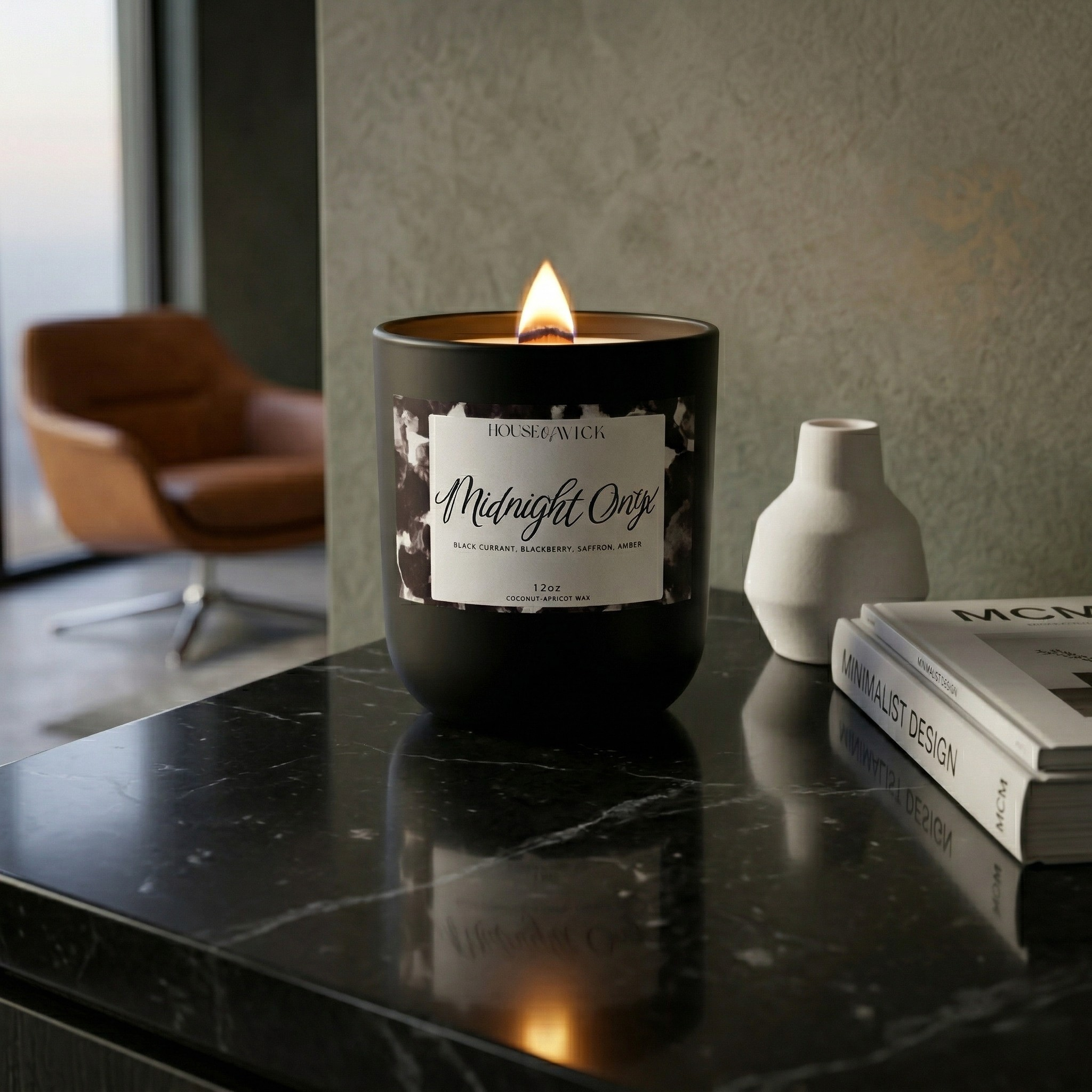 Lit House of Wick Midnight Onyx 12 oz black jar candle resting on a dark marble counter in a modern living room with a brown leather chair in the background.