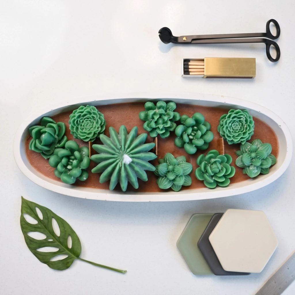 Overhead flat lay of the House of Wick Succulent Garden candle showing layered green wax succulents in an oval bowl, styled with accessories