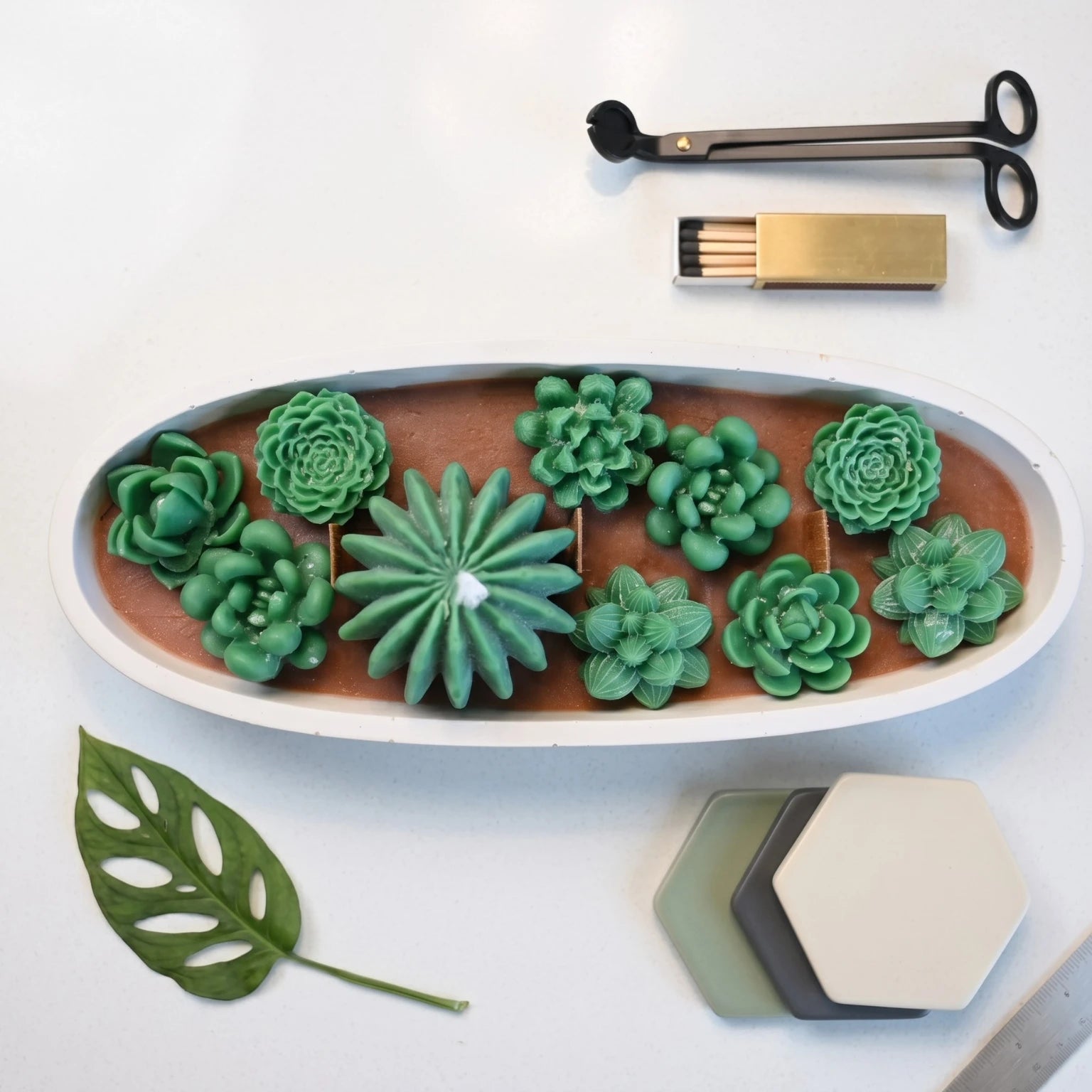 Overhead flat lay of the House of Wick Succulent Garden candle showing layered green wax succulents in an oval bowl, styled with accessories