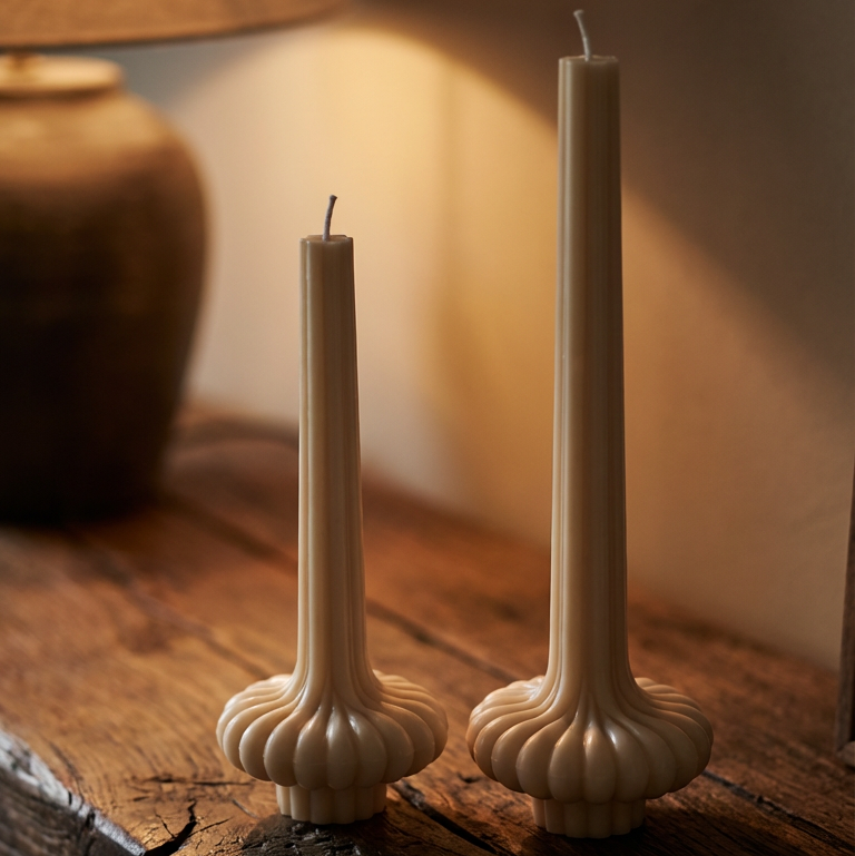 Tall sculptural vase pillar candles placed on a wooden table with warm ambient lighting for cozy modern home decor.