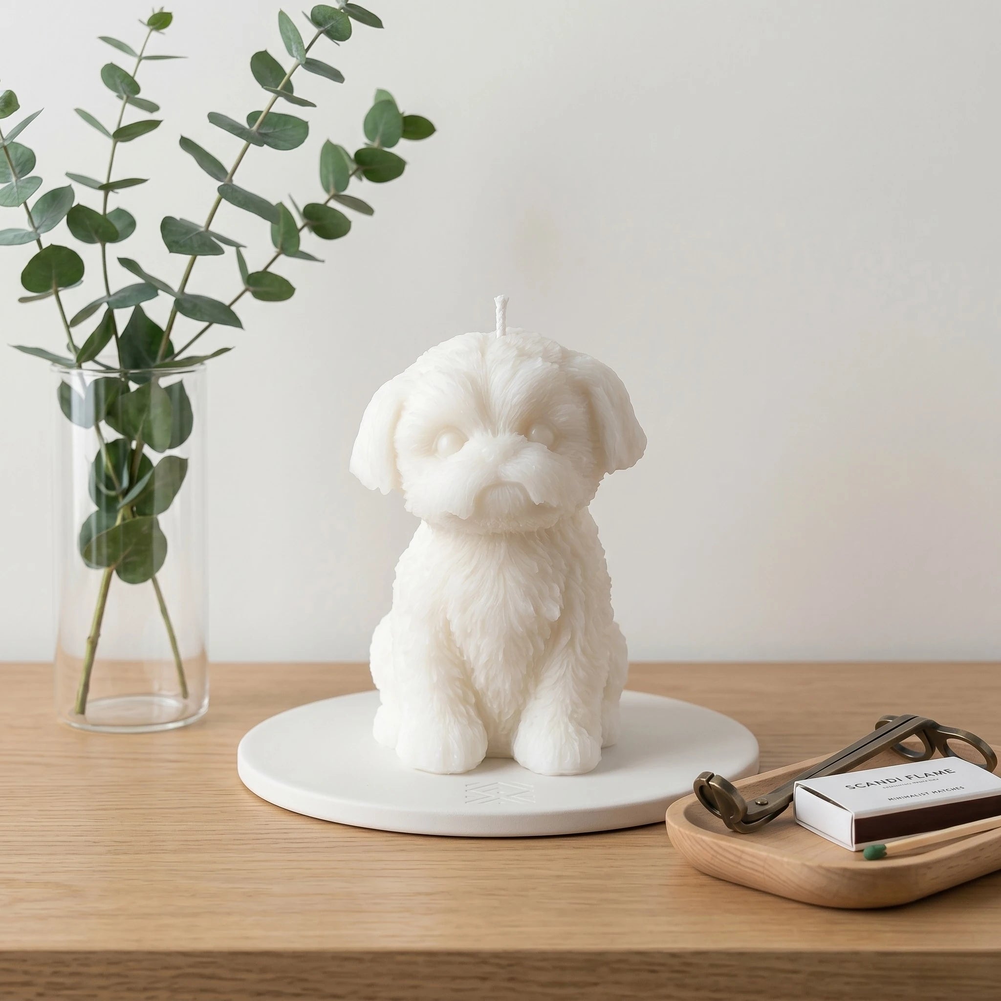 White Shih Tzu puppy candle lifestyle on wood table with palm leaf and lamp