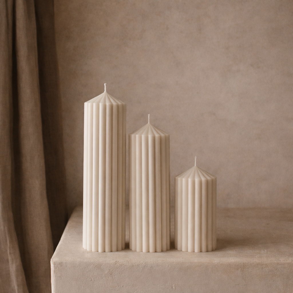 Set of ribbed pillar candles in neutral soy wax displayed on a minimal pedestal creating a soft modern home decor aesthetic.
