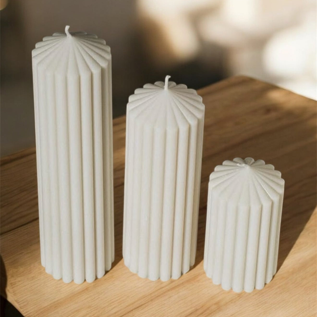 Ribbed pillar candle trio placed on a wooden table in warm natural light showcasing sculptural texture and minimalist home styling.

