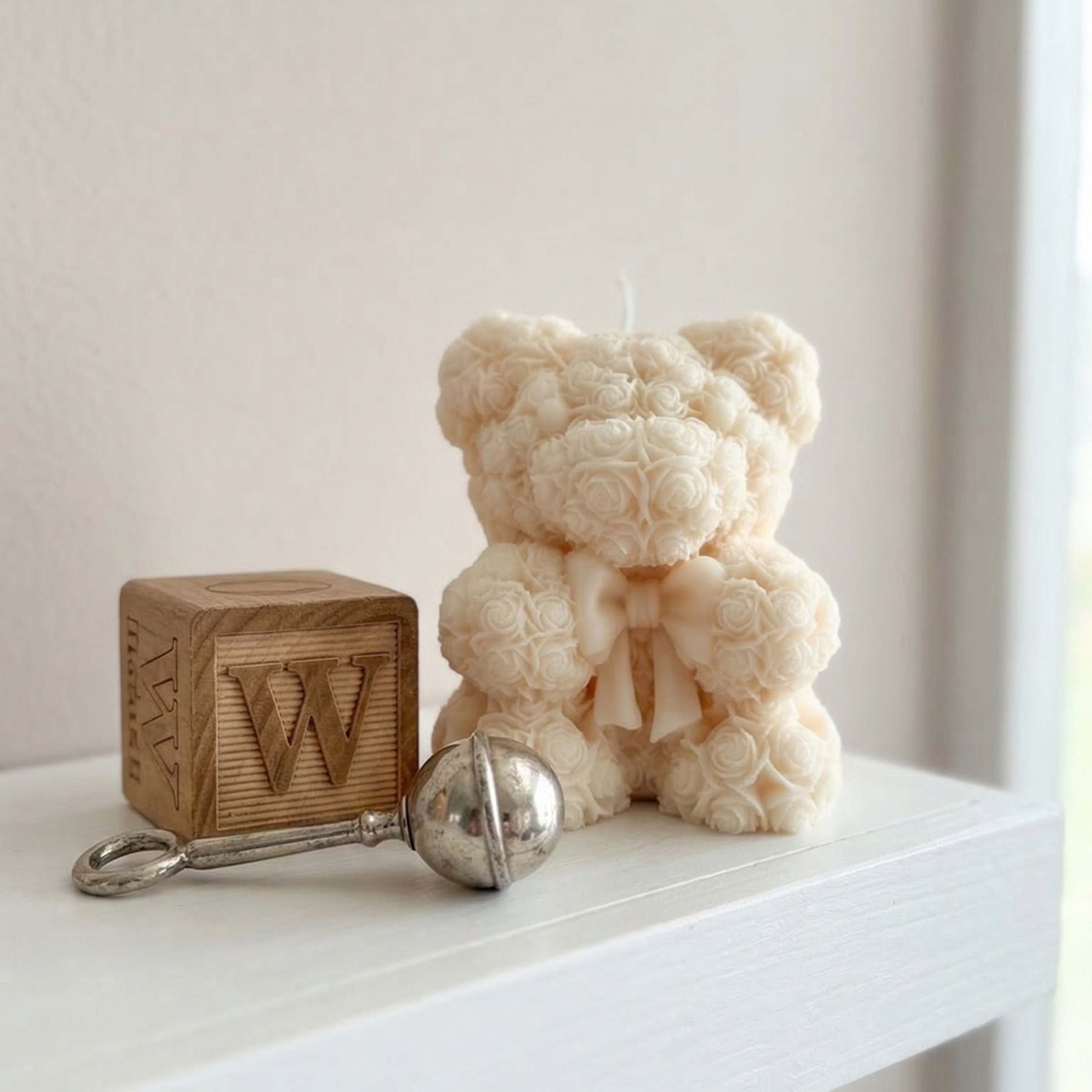 Neutral teddy bear candle with bow placed on a white shelf with wooden blocks and soft decor elements
