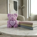 Purple teddy bear candle with heart detail placed on a marble table with books in a modern living room setting