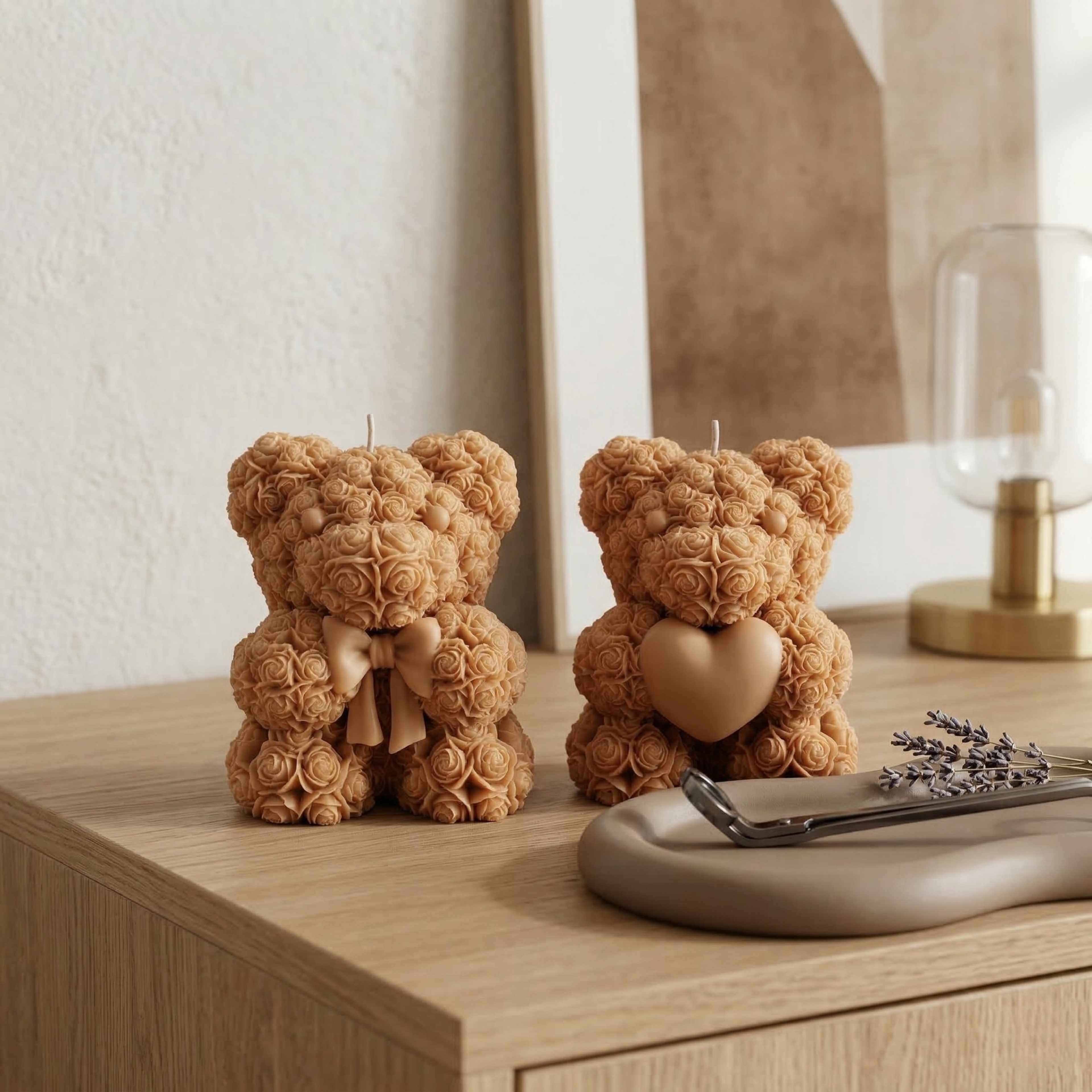 Two beige teddy bear candles with bow and heart placed on a wooden table with minimal decor accents
