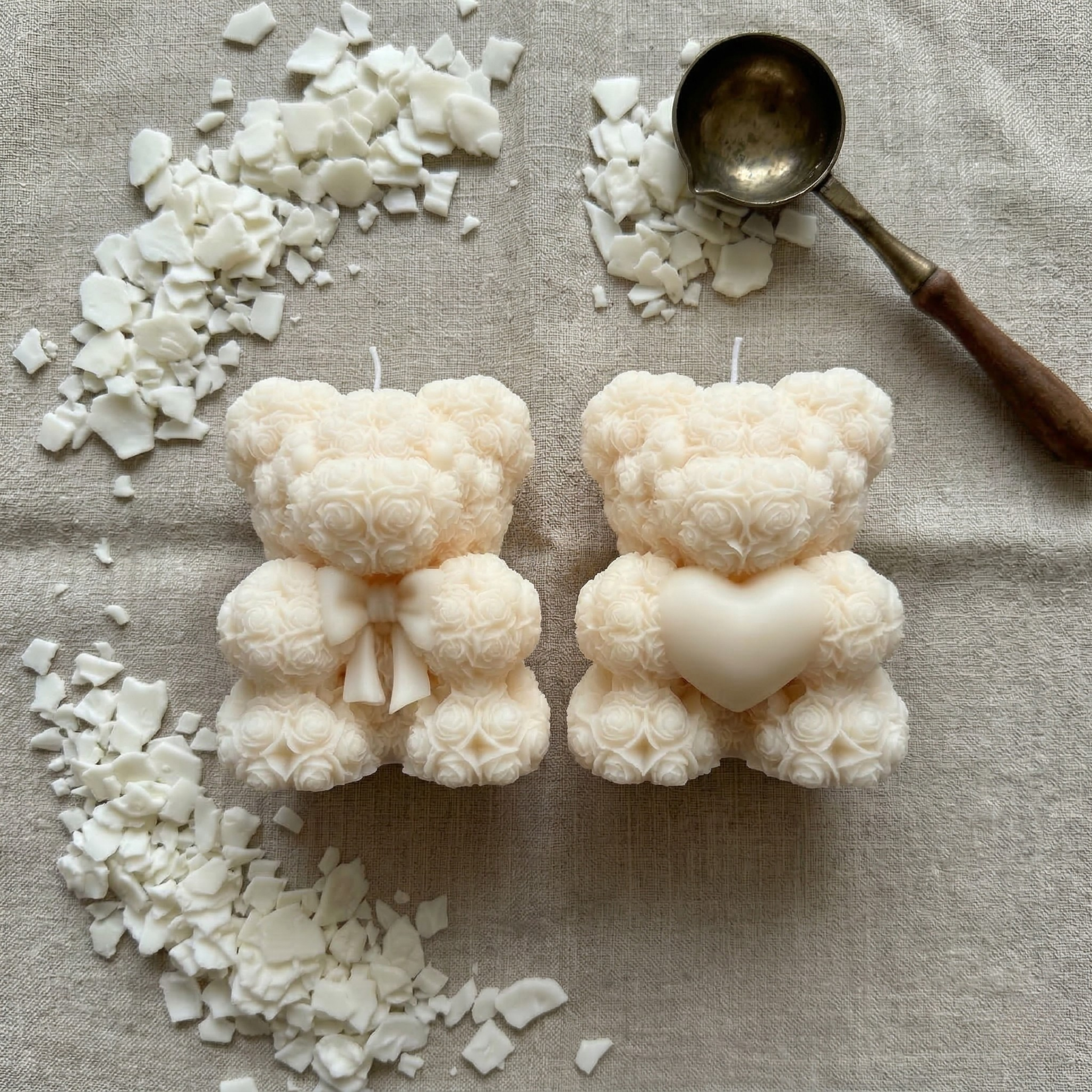 Two handmade teddy bear candles with bow and heart surrounded by soy wax pieces in a flat lay composition
